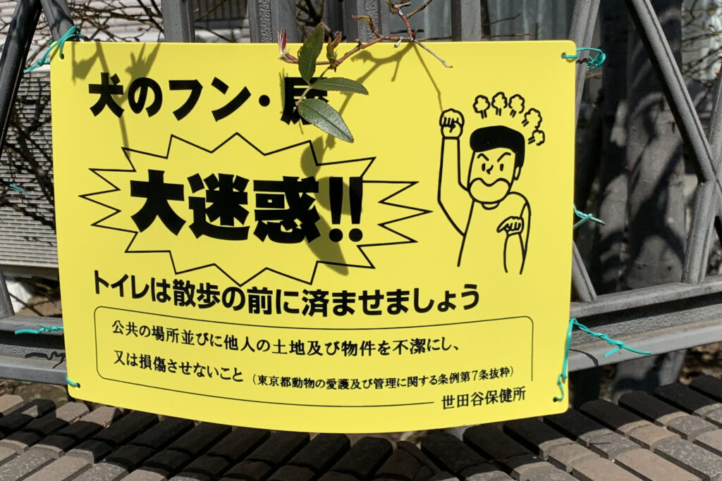 Yellow sign with black text from Setagaya: cartoon of an angry man on the right.
Main text: Dog excrection: It's a huge problem (in the center and in big letters). Get your dog to use the toilet before walking. Don't allow or leave public or private places to become unsanitary.
Encouraging dog owners to have their dog's go the the bathroom before the walk, but otherwise to make sure the clean up after their dog's excretions.